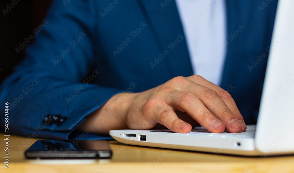 Close-up of the hands of a well-dressed man in a blue suit and a white shirt using a laptop at a desk. With a smartphone. Close-up of the hands of a well-dressed man in a blue suit and a white shirt using a laptop at a desk. With a smartphone.