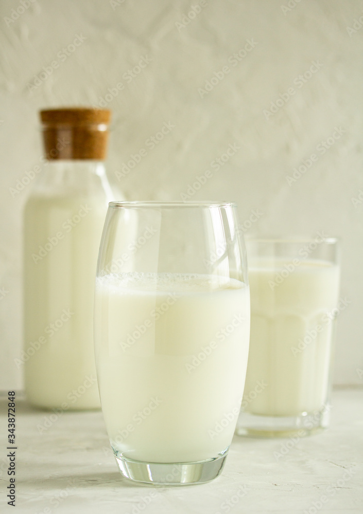 Milk in a transparent glass on a light gray background on the background of a bottle with milk and a glass with milk Milk in a transparent glass on a light gray background on the background of a bottle with milk and a glass with milk