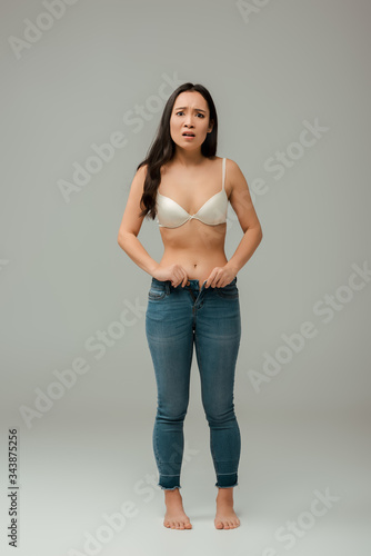 shocked and overweight asian girl wearing jeans on grey