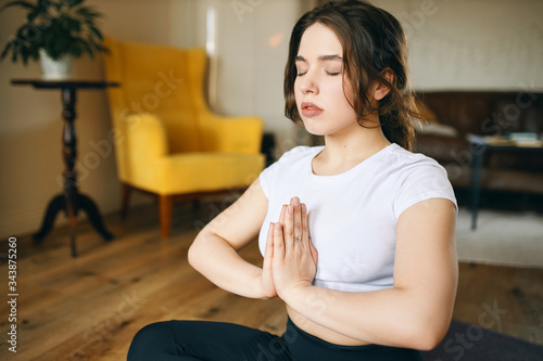 Attractive plus size young woman practicing meditation in living room to achieve mentally calm and stable state, keeping eyes closed. Mindfulness, self-awareness, peace, balance and harmony concept © Anatoliy Karlyuk