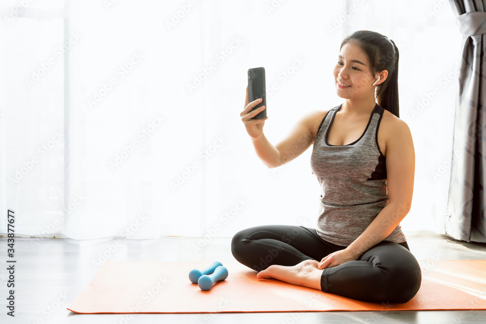Smiley Asian woman wearing sportswear sitting orange mat and take a photo of yourself while exercising. Smiley Asian woman wearing sportswear sitting orange mat and take a photo of yourself while exercising.