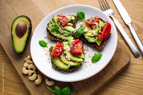 Avocado sandwich with tomatoes, basil, garlic and cashew nuts. White plate and wooden background.