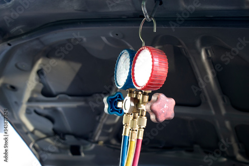 Pressure gauges with colorful pressure hose for car air condition system hanging under hood.