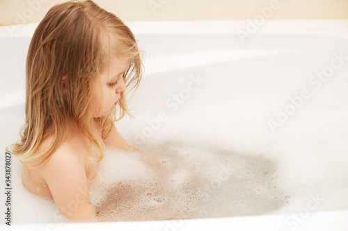 Funny little baby girl with blond hair playing with foam in a bath tub. girl takes a bath
