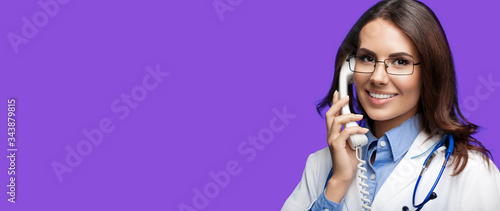 Portrait picture of happy smiling young doctor talking on phone, against purple violet background. Copy space for some sign, slogan or advertising text. Medical call center service. photo