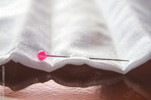 Pink needle pin on white fabric close-up.