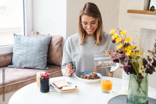 Photo of cheerful young woman eating cereal while having breakfast