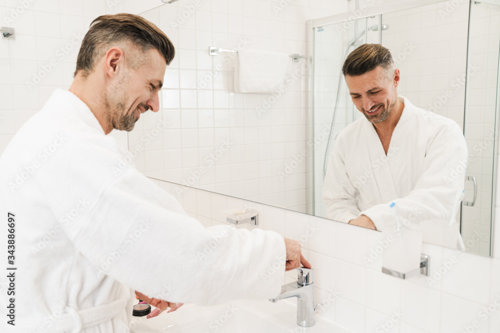 Fototapeta premium Photo of cheerful caucasian man washing and smiling in bathroom