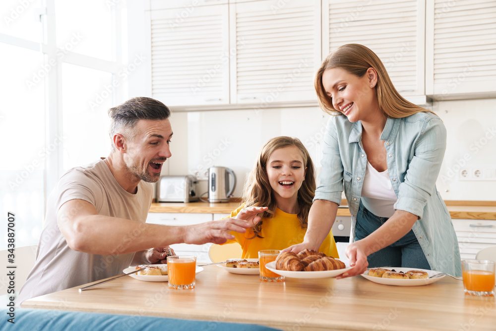 Photo of happy family eating croissants while having breakfast