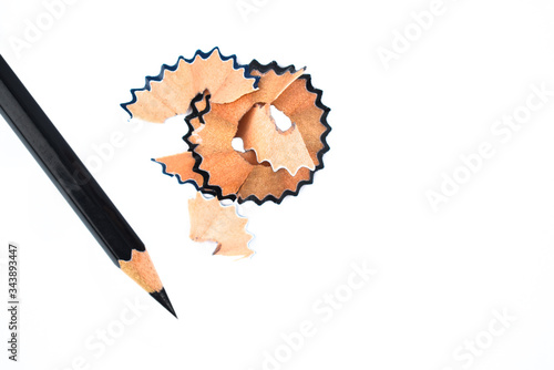 Photograph of some pencil shavings placed beside a black color wood pencil