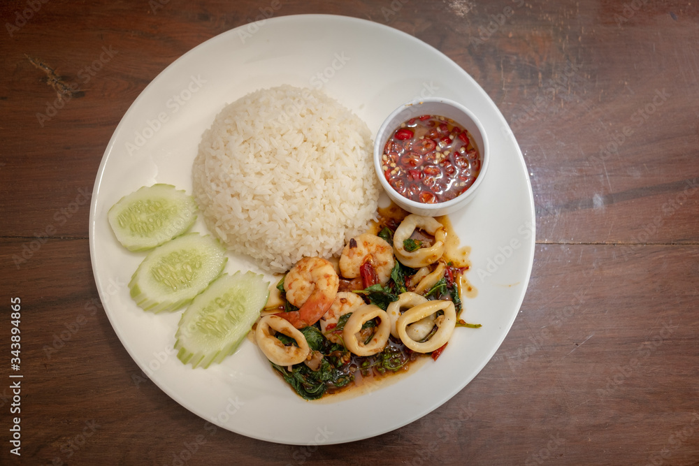 Pad Kra Pao Seafood(Thai food) - fried shrimps and squids with holy basil beside cooked rice and Chilli Fish Sauce - Stock Photo