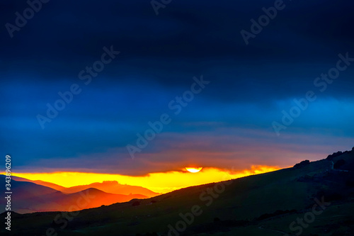 Sun setting over Silhouetted Mountains, Clouds 