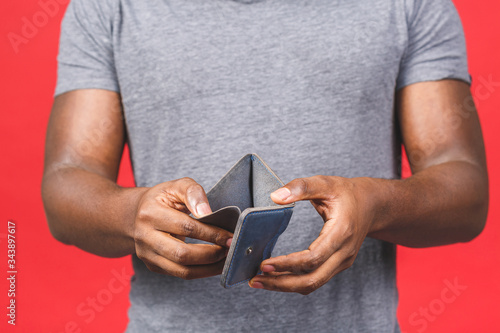Poverty crisis concept. Upset african american young bearded man in casual holding empty wallet over red background.