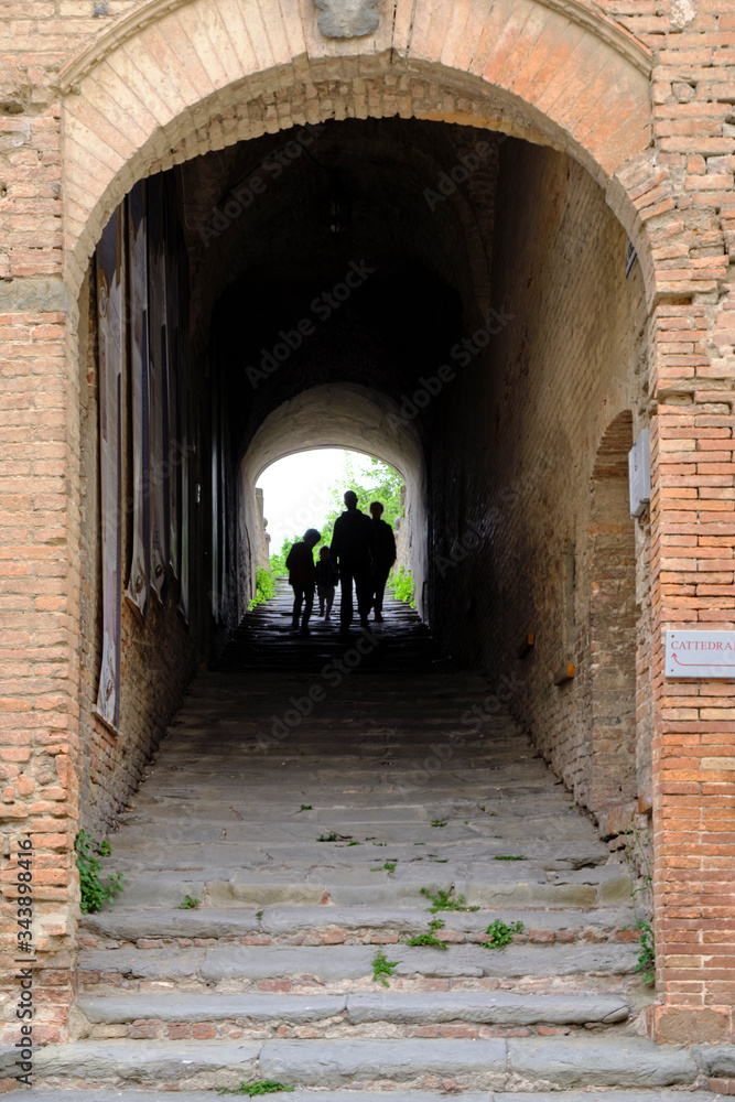 Pilgrims walkings under arcades on stairs in little town San Miniato. Solo Backpacker Trekking on the Via Francigena from Lucca to Siena. Walking between nature, history, churches,