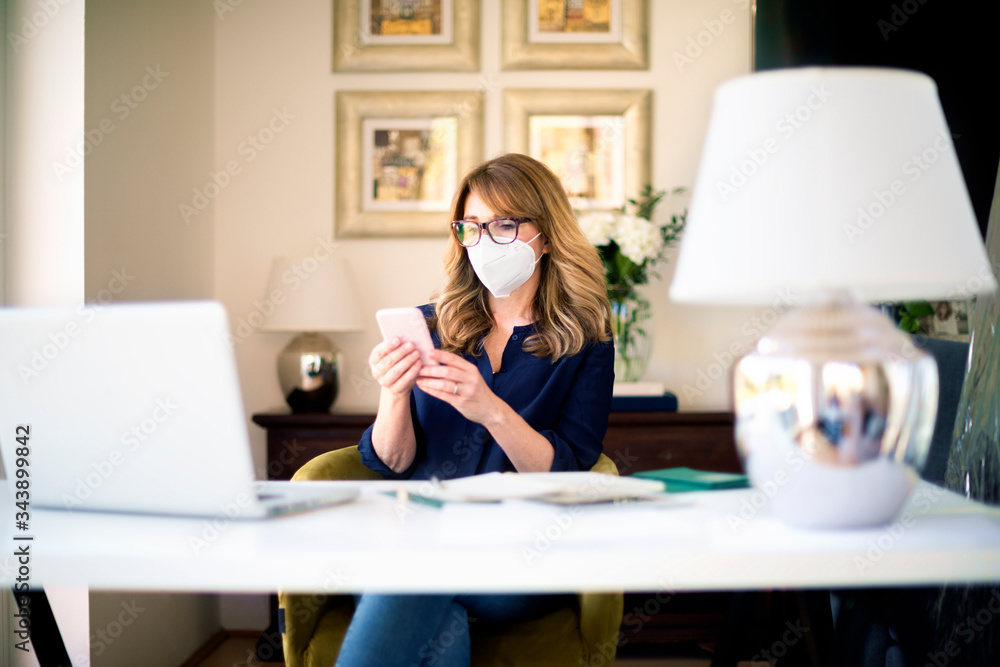 Mature woman wearing face mask while working from home during coronavirus pandemic Mature woman wearing face mask while working from home during coronavirus pandemic