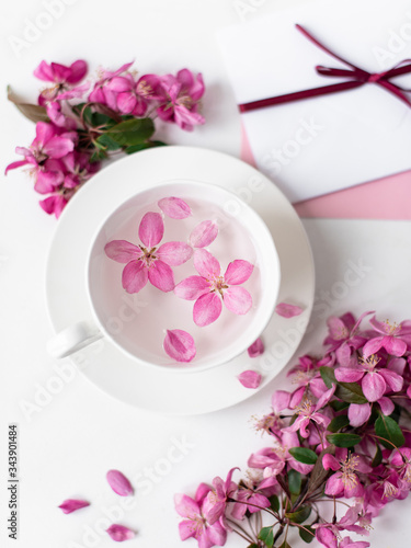 Spring background for the inscription, pink flowers, sakura cherry blossoms, letters, a cup with water and flower petals, top view, frame, copy space flat lay 