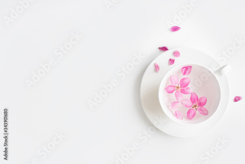 Spring background for the inscription, pink flowers, sakura cherry blossoms, cup with water and flower petals, fashion trend of the year, top view, creative banner, copy space flat lay