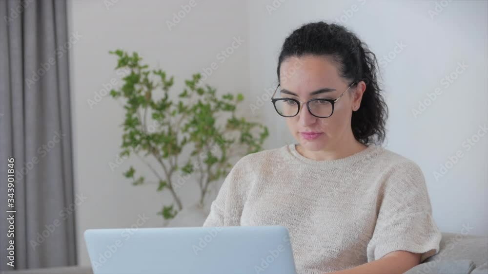 Young caring caucasian woman freelancer putting on glasses before starting to work on a laptop,looking at the camera. Serious woman looks at the camera and begins to work at a laptop. Young caring caucasian woman freelancer putting on glasses before starting to work on a laptop,looking at the camera. Serious woman looks at the camera and begins to work at a laptop.