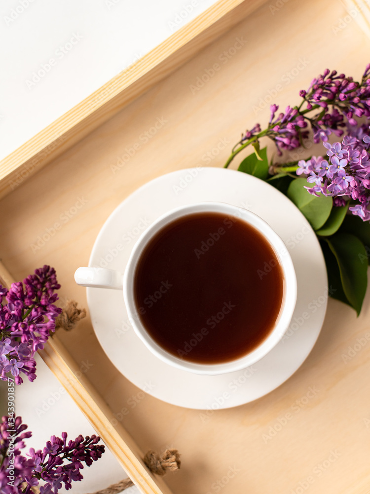 porcelain cup with coffee, cocoa, spring breakfast on a wooden tray. Branches and flowers of lilac, violet color, on a white background. Minimalistic design porcelain cup with coffee, cocoa, spring breakfast on a wooden tray. Branches and flowers of lilac, violet color, on a white background. Minimalistic design