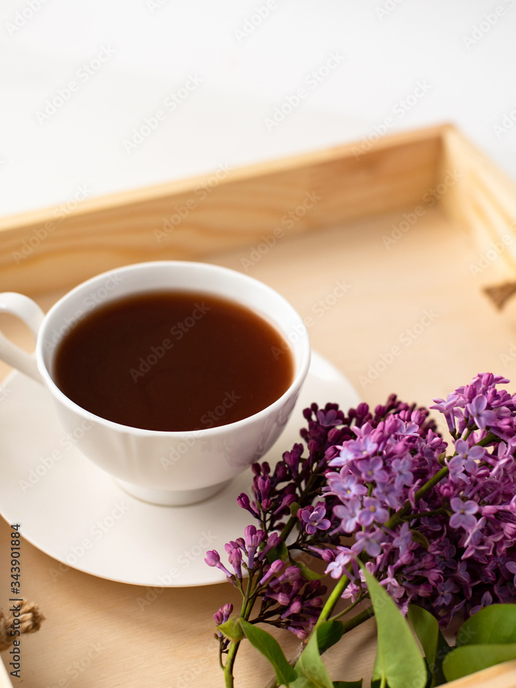 porcelain cup with coffee, cocoa, spring breakfast on a wooden tray. Branches and flowers of lilac, violet color, on a white background. Minimalistic design porcelain cup with coffee, cocoa, spring breakfast on a wooden tray. Branches and flowers of lilac, violet color, on a white background. Minimalistic design