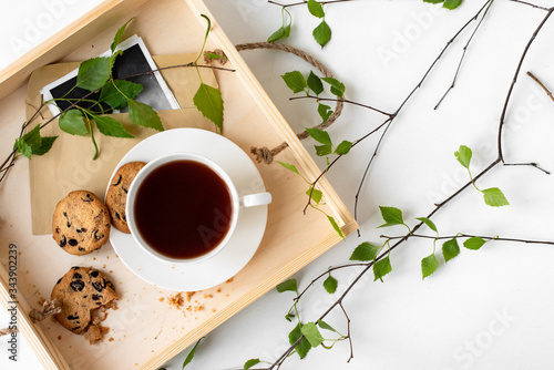 A cup of coffee, tea, chocolate chip cookies, a meal on a wooden tray. Branches with leaves, greenery, on a white background. Unity with nature.Minimalistic design, creative banner,flat lay, top view