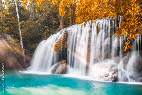 Waterfall and blue emerald water in autumn forest with sun flare and sunlight in morning. Erawan Waterfall step 2nd. Beautiful nature rock waterfall steps in rainforest at Kanchanaburi, Thailand