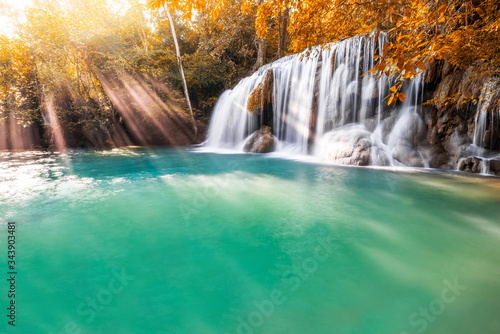 Waterfall and blue emerald water in autumn forest with sun flare and sunlight in morning. Erawan Waterfall step 2nd. Beautiful nature rock waterfall steps in rainforest at Kanchanaburi  Thailand