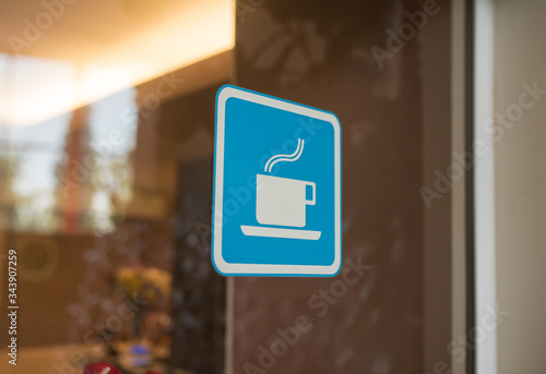 Close up to sticker of symbol coffee shop on glass background. Cafe wallpaper view. sticker on the window with a picture of a cup of coffee. coffee bar sticker on a glass blue