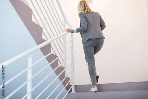 Business woman going up the stairs. Close up view of blonde woman in gray walking up on the stair, business promotion concept.