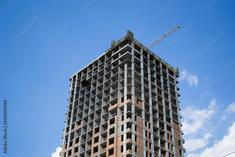 Construction of a multi-storey residential building. Construction crane. Against the blue sky