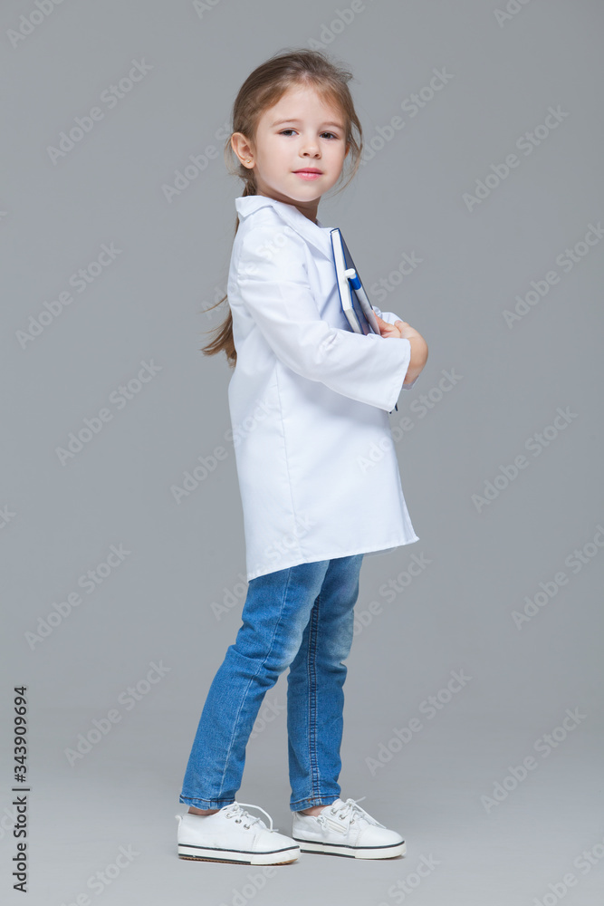 Adorable child girl uniformed as doctor is holding medical record isolated on grey background Adorable child girl uniformed as doctor is holding medical record isolated on grey background