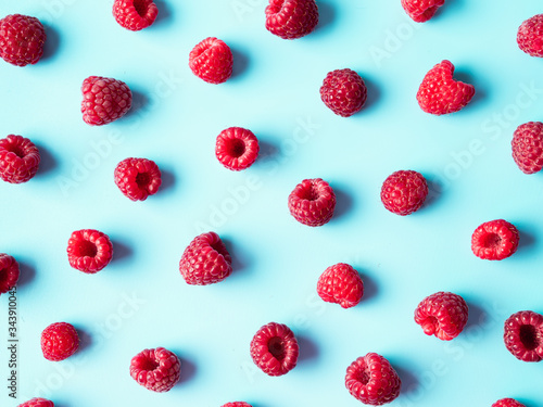 Pattern of ripe red raspberry on blue background. Organic raspberries creative layout. Top view or flat lay. Vegan food, detox concept