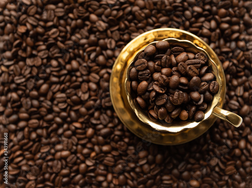 Golden cup on saucer filled with coffee beans on blurred background full of coffee beans