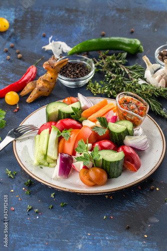 Plate with fresh vegetable sliced salad with cucumber, tomato, pepper and celery on white plate on blue background