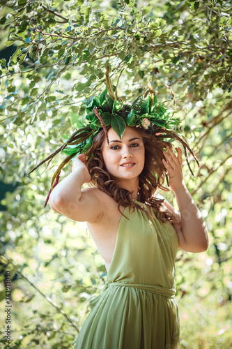 Beautiful young woman in a green dress and a wreath in a sunny forest