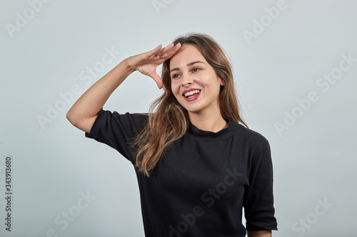Wallpaper Mural Cute young brunette woman in black t-shirt, blue jeans with belt on gray background, happy smiling girl holding the palm of her hand on her forehead, gazing into the distance Torontodigital.ca