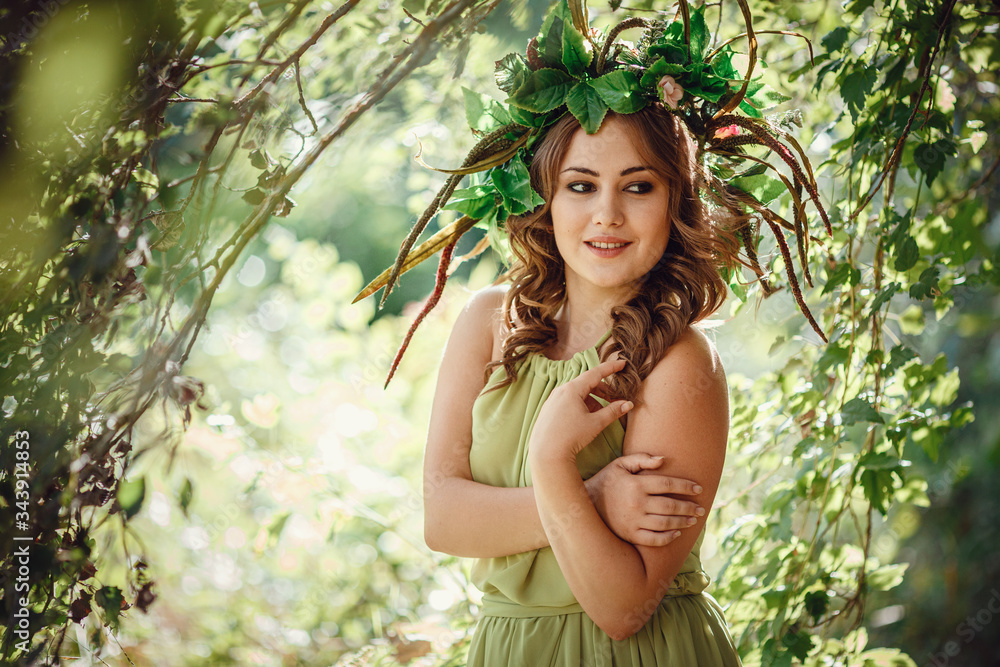 Beautiful young woman in a green dress and a wreath in a sunny forest Beautiful young woman in a green dress and a wreath in a sunny forest