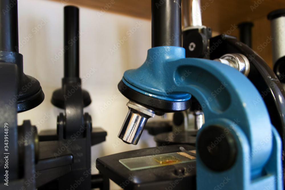 Close up blue and black microscopes stand on cabinet shelf. Laboratory equipment kit. Science and biology concept. Close up blue and black microscopes stand on cabinet shelf. Laboratory equipment kit. Science and biology concept.