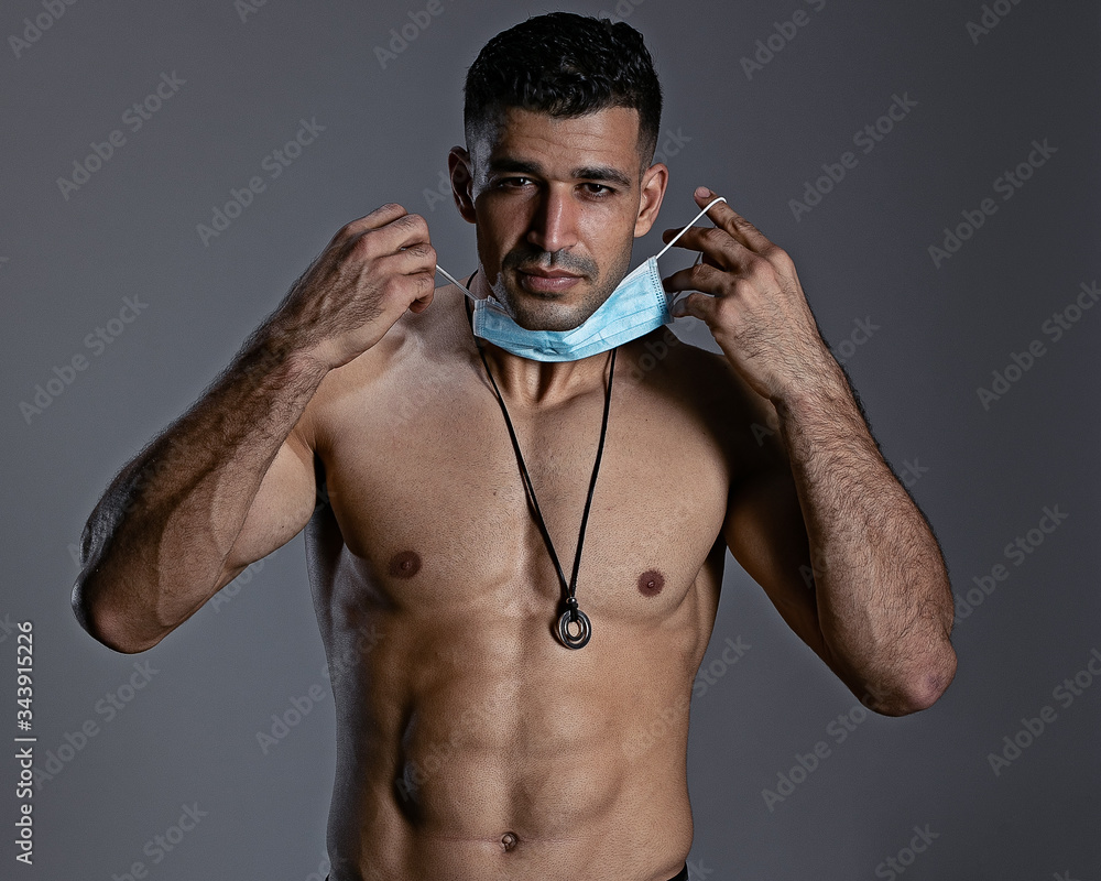 Fototapeta premium Male bodybuilder in a medical mask stands torso.