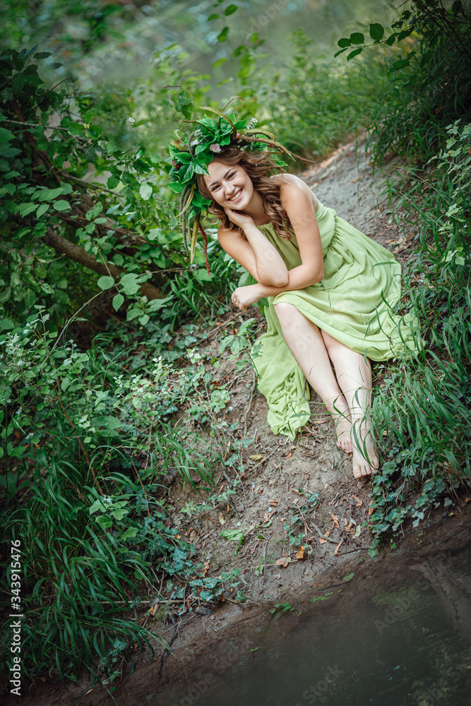 Beautiful young woman in a green dress and a wreath in a sunny forest Beautiful young woman in a green dress and a wreath in a sunny forest