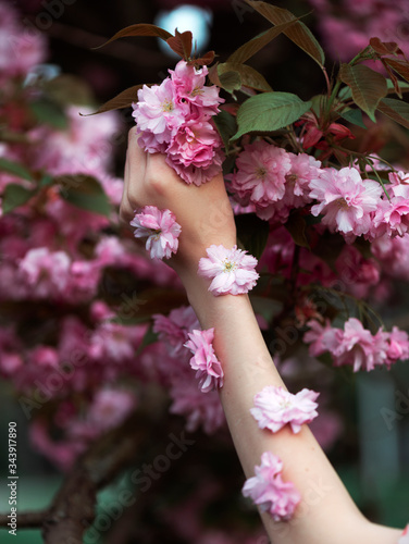 Fashion art woman hand in summer and flowers on her hand, against a background of pink flowers