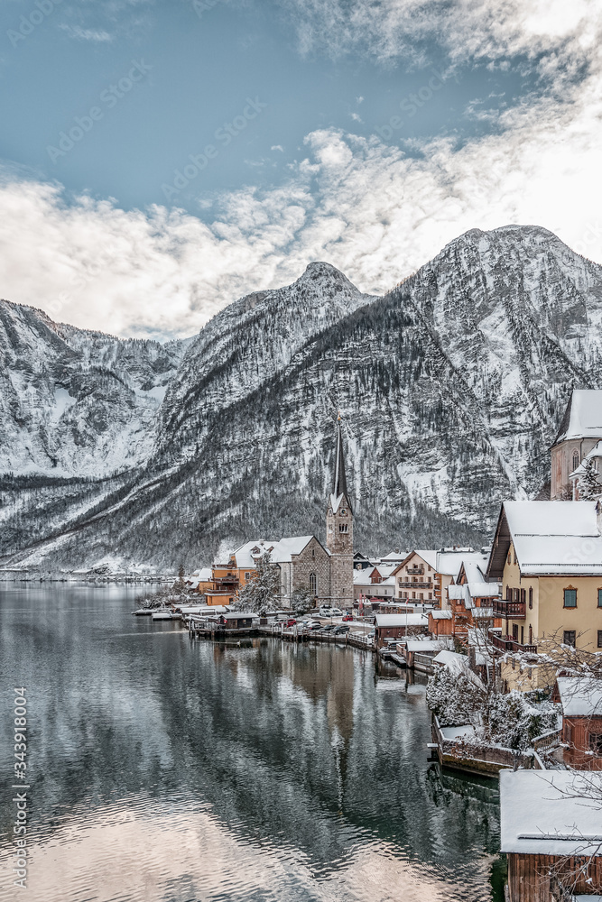 Fototapeta premium Snowy village Hallstatt by lake at foot of snow mountain with clear sky in winter in Austria