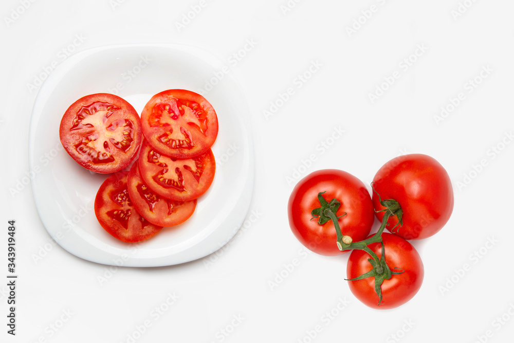 Sliced tomato on a white plate. White isolated background. Nearby are several tomatoes. Flat lay. Copy space. Sliced tomato on a white plate. White isolated background. Nearby are several tomatoes. Flat lay. Copy space.