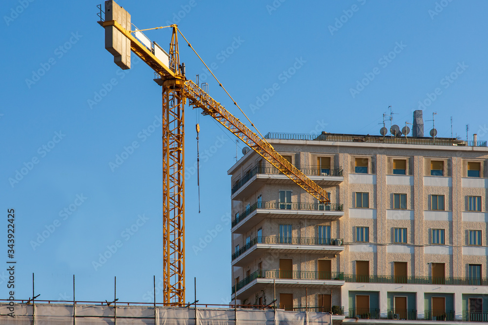 A morning walk to the residential area of the city. Maintenance work on a building and a yellow tower crane on the background of the clear August sky. A morning walk to the residential area of the city. Maintenance work on a building and a yellow tower crane on the background of the clear August sky.