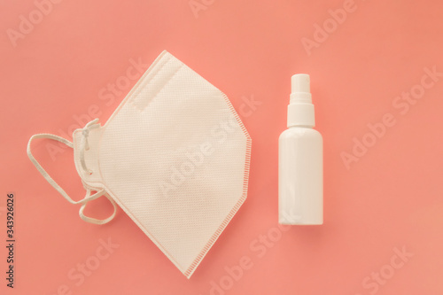 Sanitizing antibacterial spray in white bottle and protective mask for infection prevention.