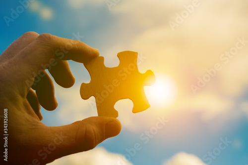 Piece of puzzle in businessman hand on sunset background, business concept, creative, cooperation, team work, partnership. Add your idea