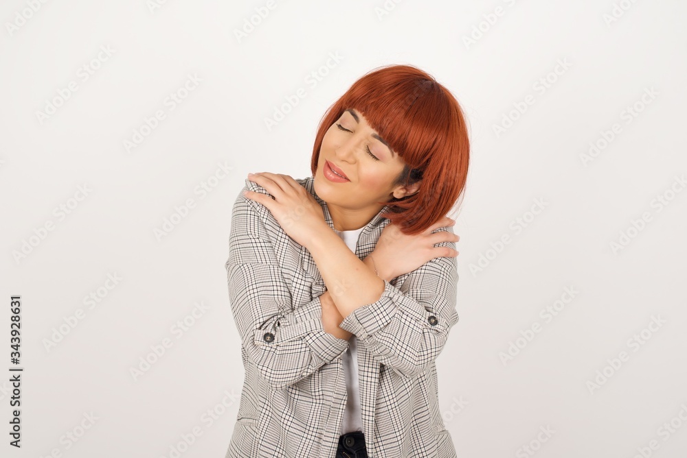Portrait of a pretty young girl hugging herself with eyes closed while standing isolated over white background Portrait of a pretty young girl hugging herself with eyes closed while standing isolated over white background
