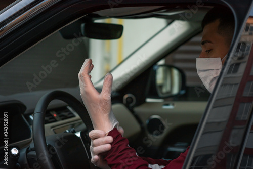 a man driving in medical mask in car puts medical gloves on a  during an epidemic, a taxi driver in a mask, protection from the virus. Driver in black car. coronavirus,infection, quarantine, covid-19