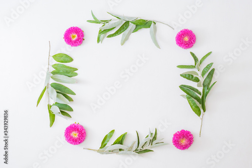 Flat lay frame of flowers and green leaves on a white background