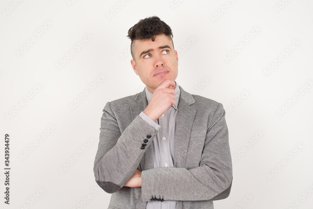 Portrait of thoughtful man keeps hand under chin, looks away trying to remember something or listens something with interest, dressed casually, poses indoors. Youth concept. Portrait of thoughtful man keeps hand under chin, looks away trying to remember something or listens something with interest, dressed casually, poses indoors. Youth concept.